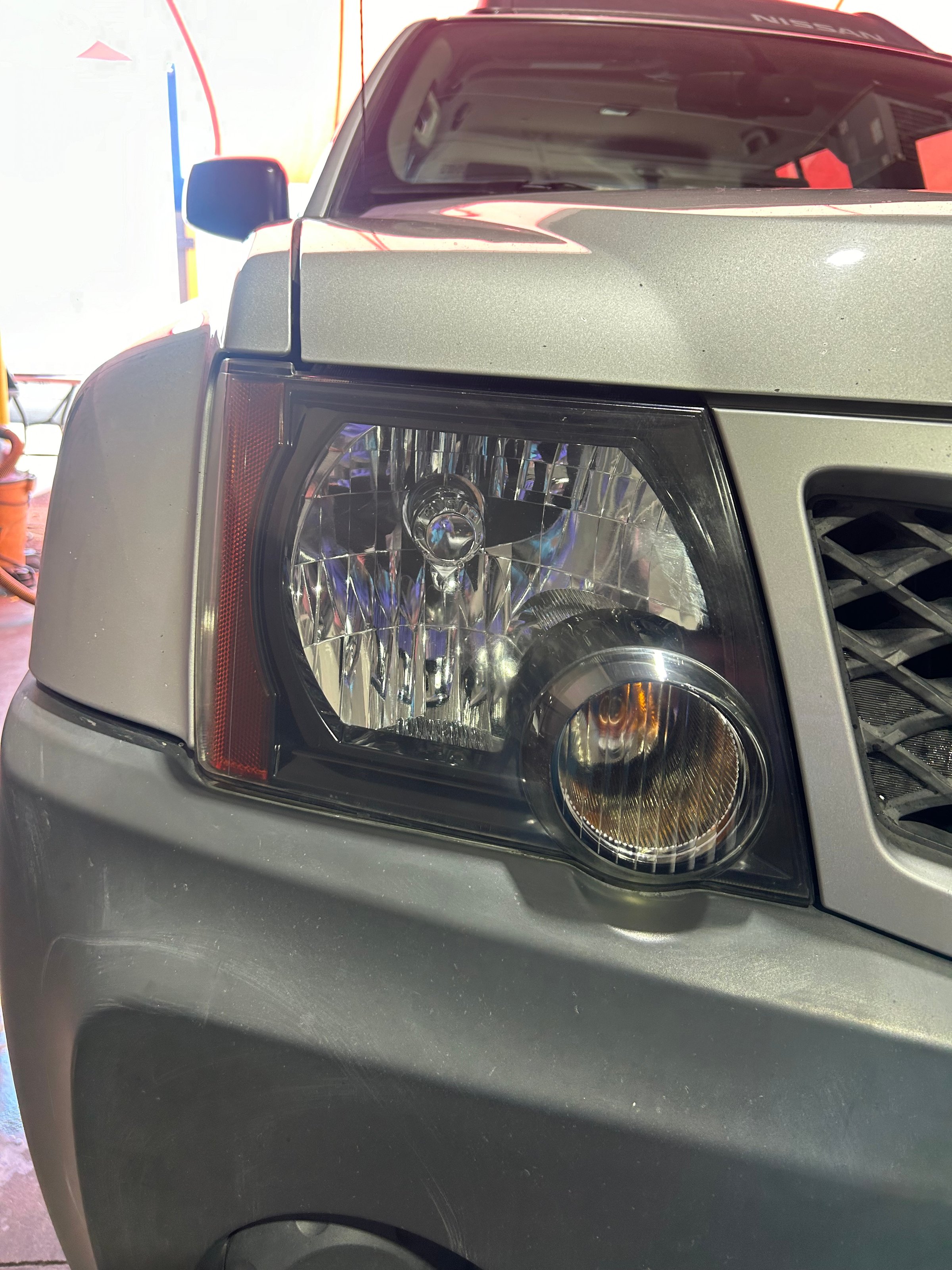 Close-up of a car's front headlight and grille, showcasing modern design details in a brightly lit setting.
