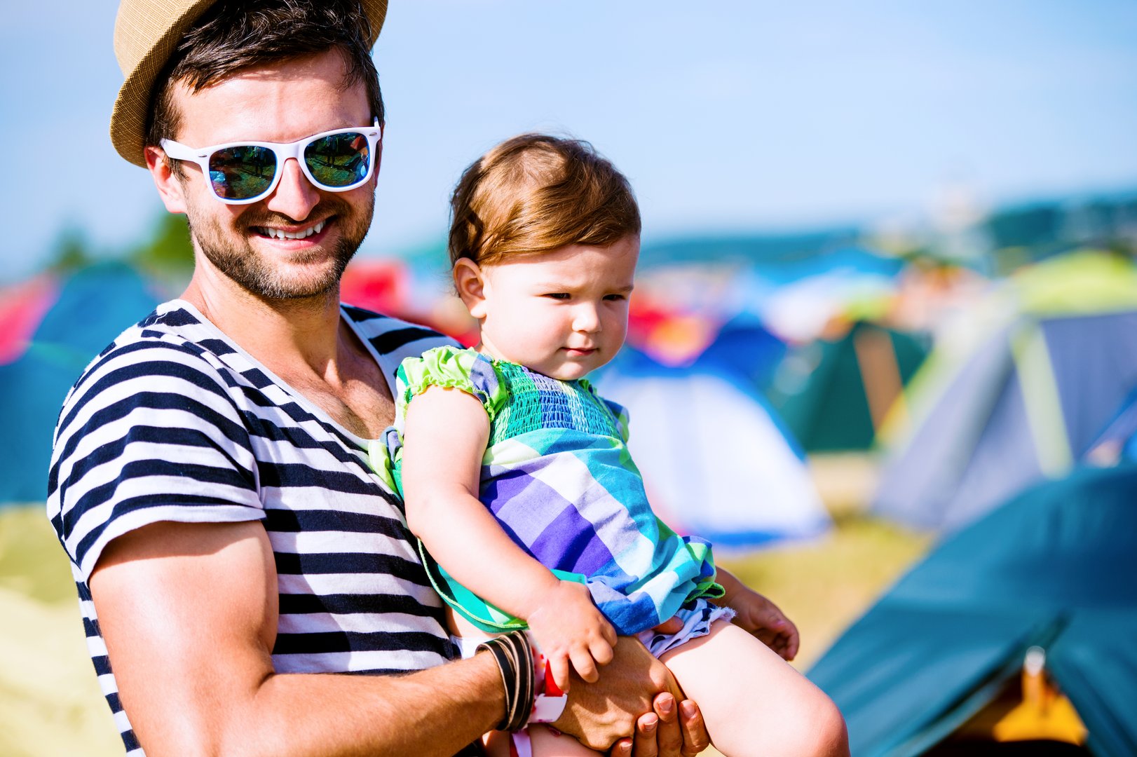 Young father with his baby daughter between tents at summer music festival