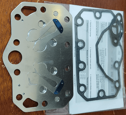 Metal gasket on a wooden surface, with a black gasket and instructions in the background.