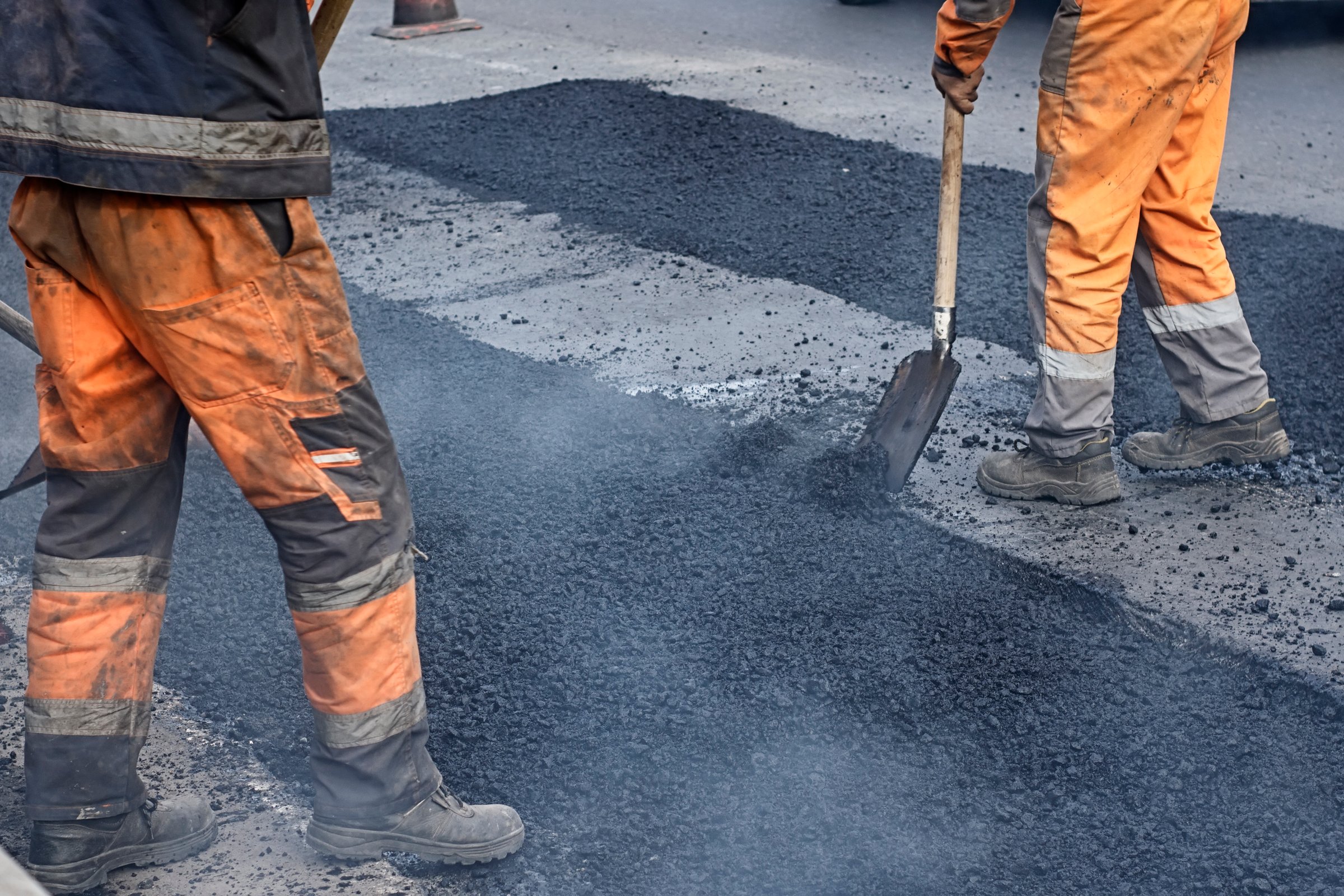 A working group of road workers renews part of the road with fresh hot asphalt and smooths it out for repair.