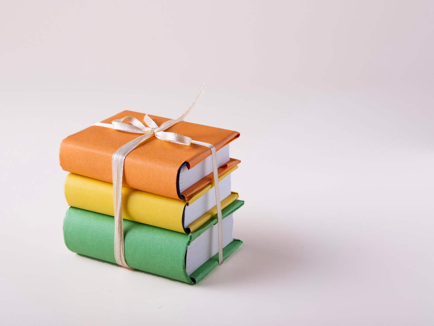 a stack of mini books in bright covers tied with a satin ribbon, on a white background, space for text