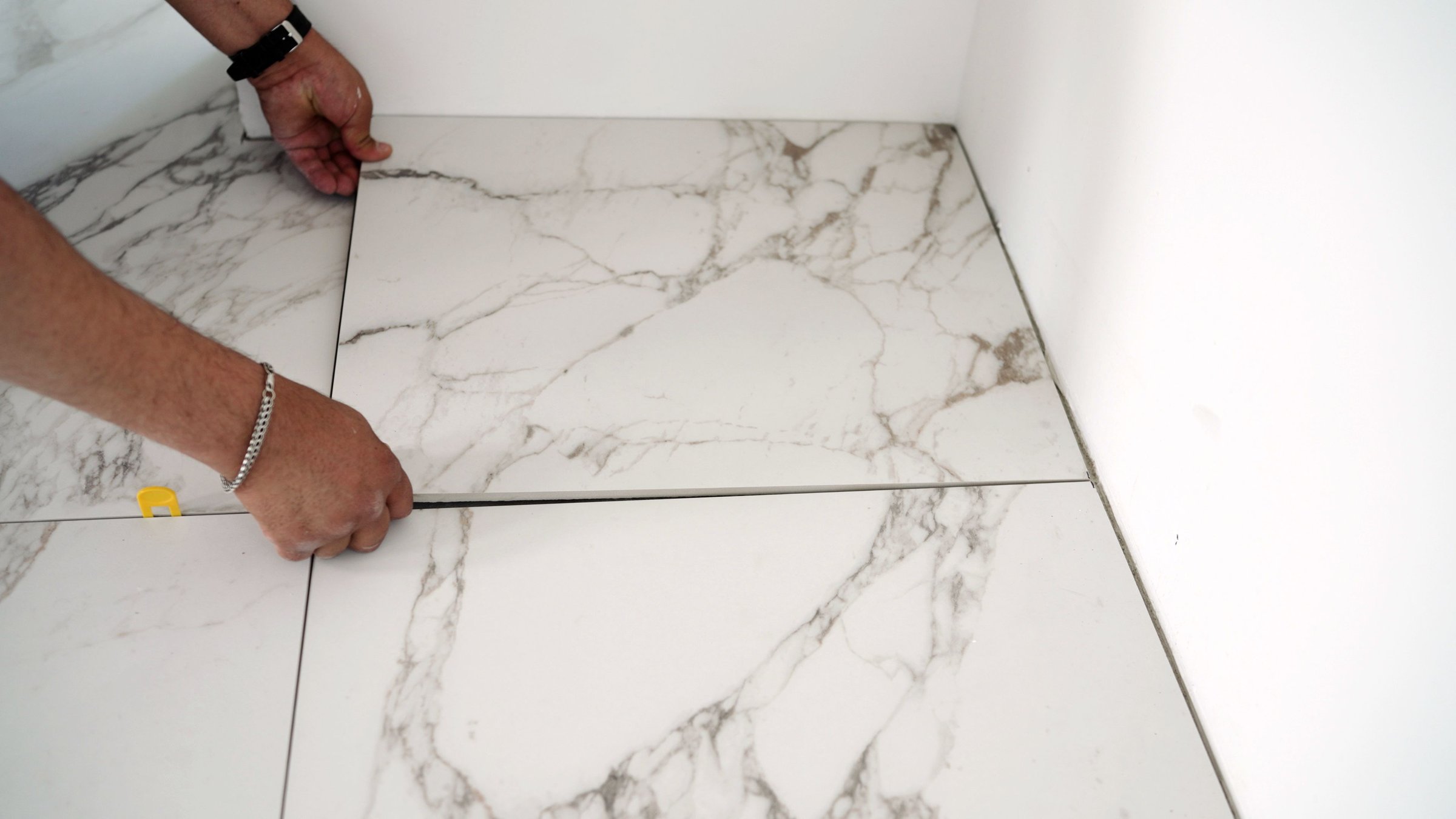 Construction worker placing large format white porcelain tiles with marble effect on the floor during renovation work