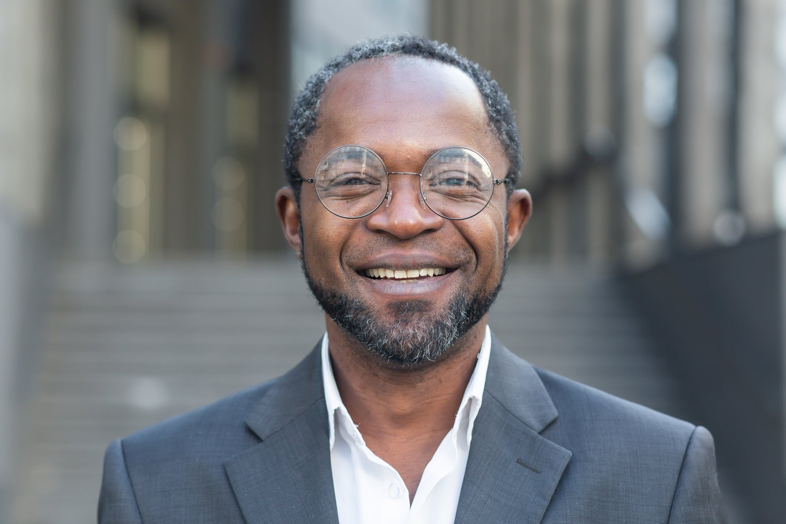 Close up photo portrait of successful and smiling African American man, businessman wearing glasses smiling and looking at camera from outside office building.