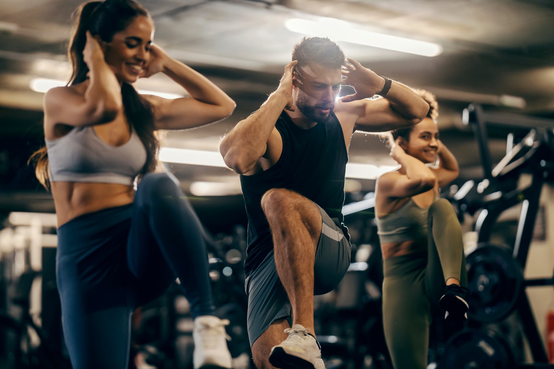 Fit friends doing high knees workout in a gym with fitness instructor.