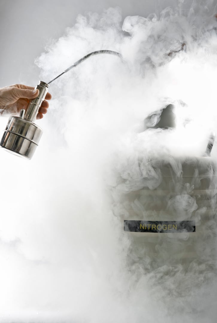 Hands of two men pour liquid nitrogen from big cask into small. Grey background. Steam of nitrogen. Cryogen
