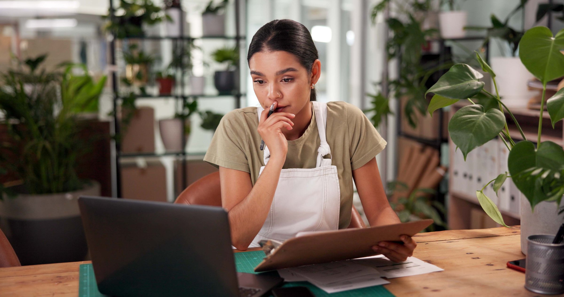 Woman, florist and clipboard with laptop at shop with stress, thinking and problem solving at small business. Person, pc and sustainability for plants with mistake, crisis and lost order on web store