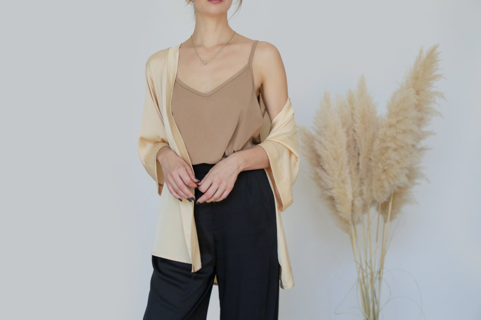 Female model wearing beige camisole cotton top and black trousers. Classic and simple summer fashion. Studio shot.