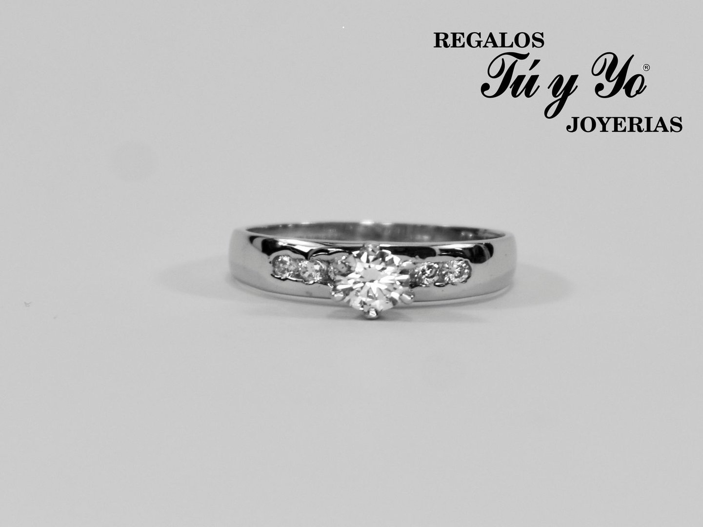Silver engagement ring with a central diamond and smaller side stones, displayed on a plain background.