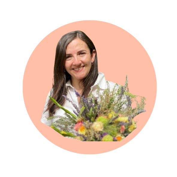 Woman smiling, holding a bouquet of assorted colorful flowers, set against a peach circular background.