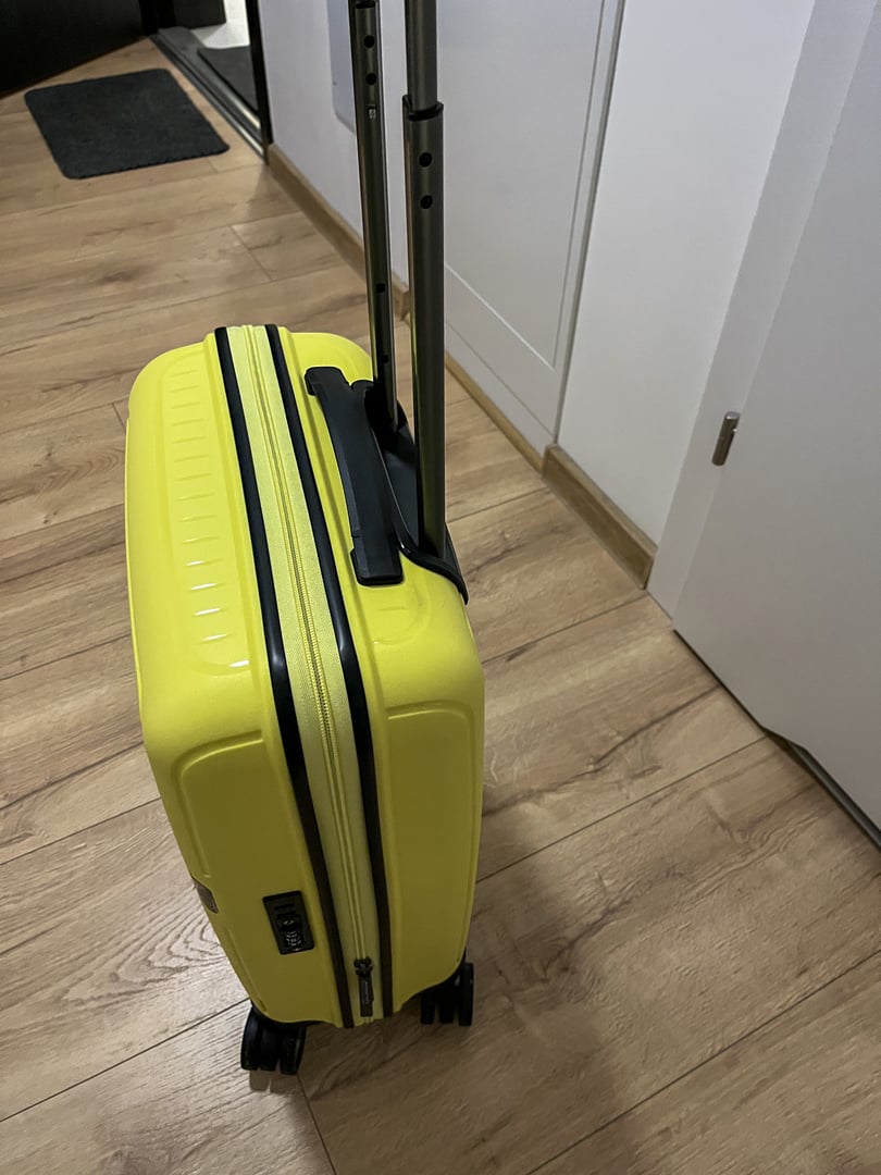 Compact yellow hardshell carry on suitcase on a wooden floor with telescopic handle and built in lock. Modern interior scene suggests travel readiness, mobility, weekend trip, airport and business use