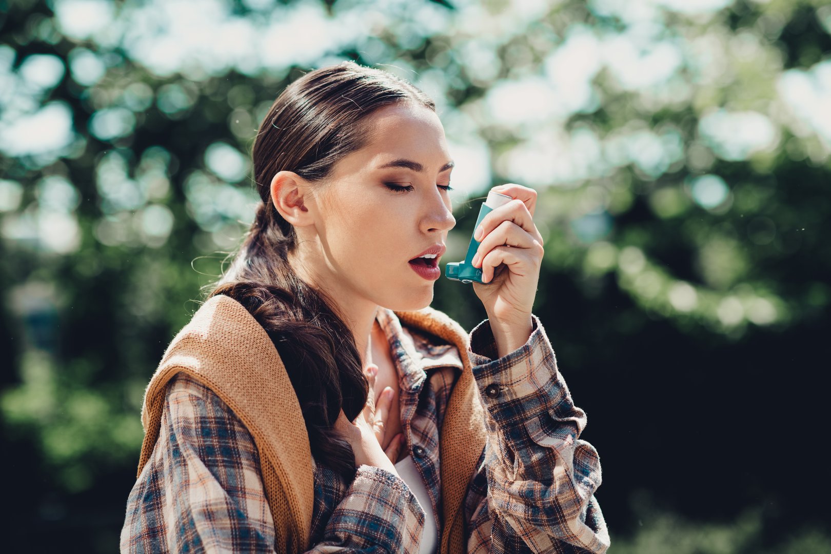 A young female uses an inhaler for asthma relief on a sunny day outdoors, showcasing health, vitality, and proactive self-care.