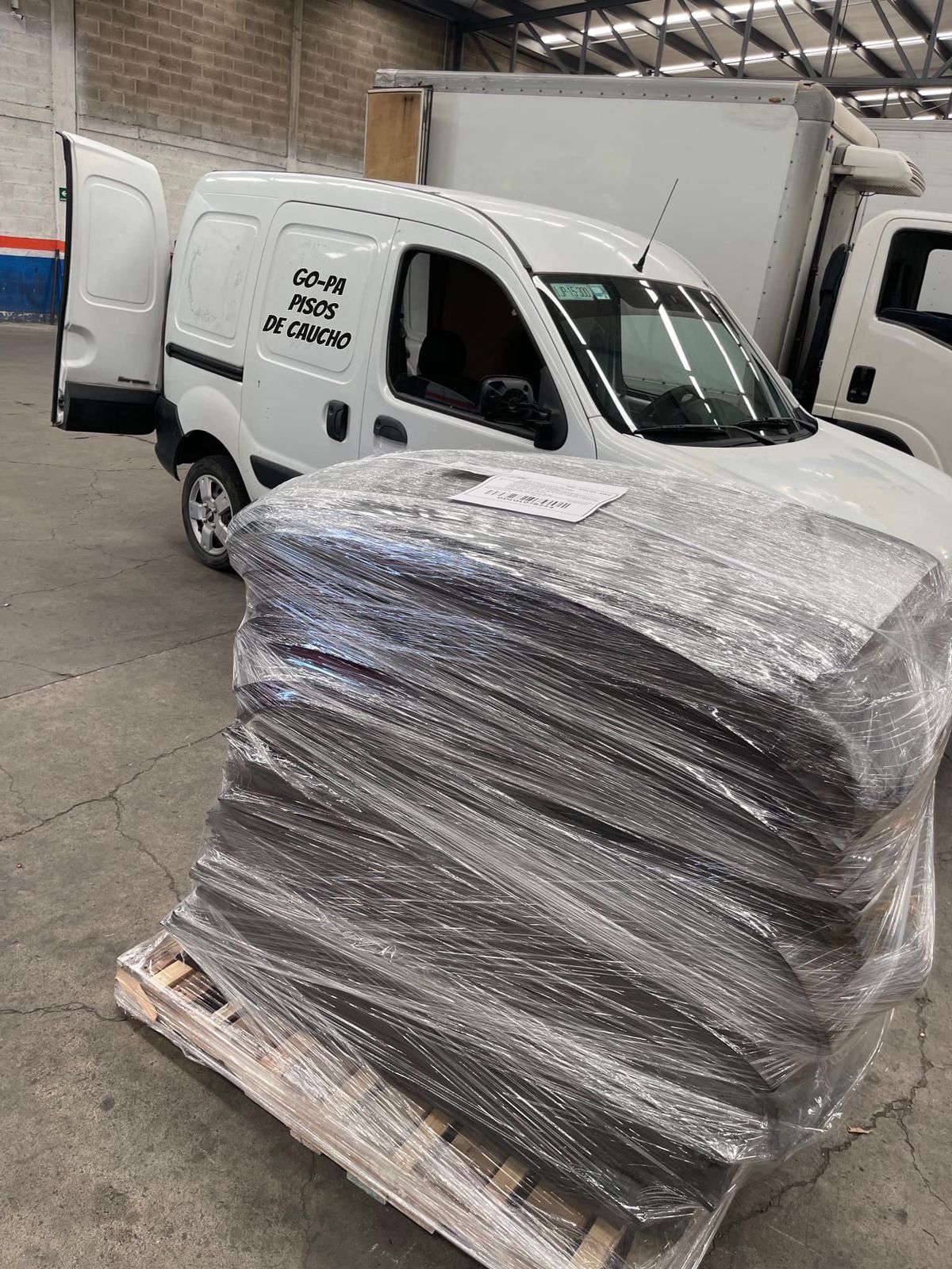 Rubber flooring sheets stacked on a pallet in a warehouse, with a delivery van in the background.