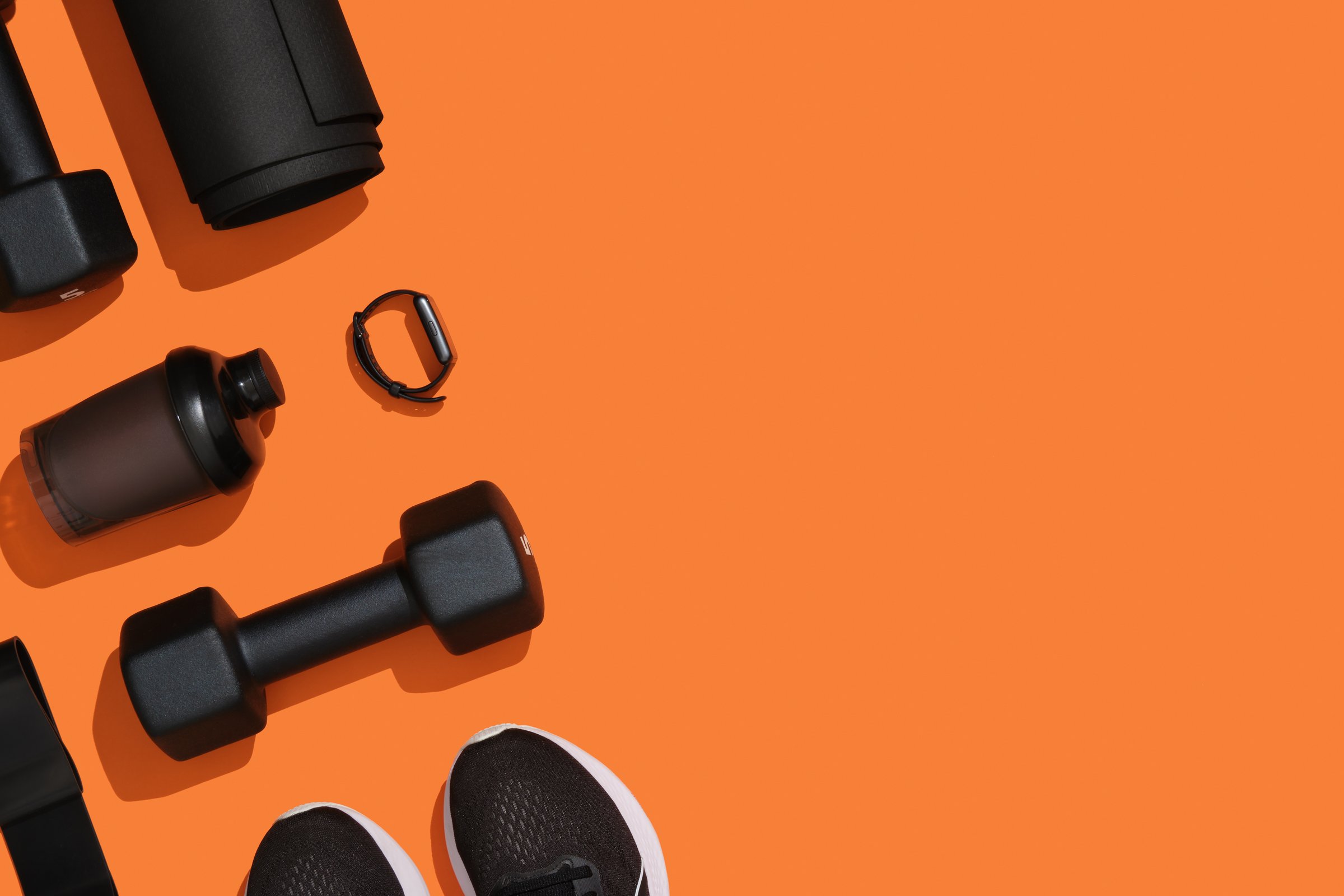 Black exercise equipment, dumbbells, mat, elastic band, fitness band, fitness band, sneakers on orange background. Fitness, sports items, healthy lifestyle. Place for your text