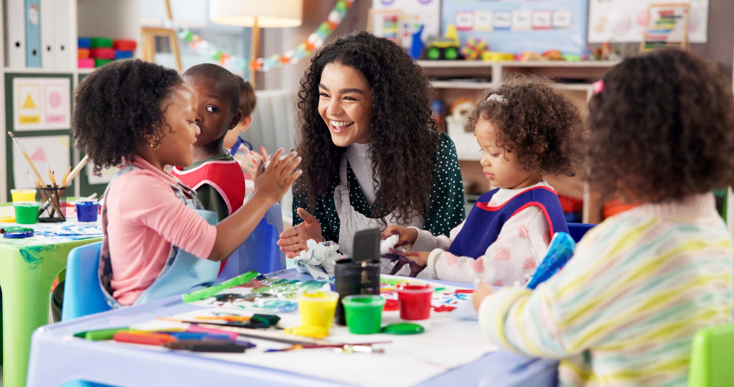 Education, children or painting with teacher in class for art, creative talent or motor skill development in preschool. Learning, students drawing or teaching happy kids for lesson or help with color