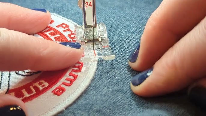Close-up of a person sewing a red and white patch onto denim fabric using a sewing machine with blue painted nails visible.