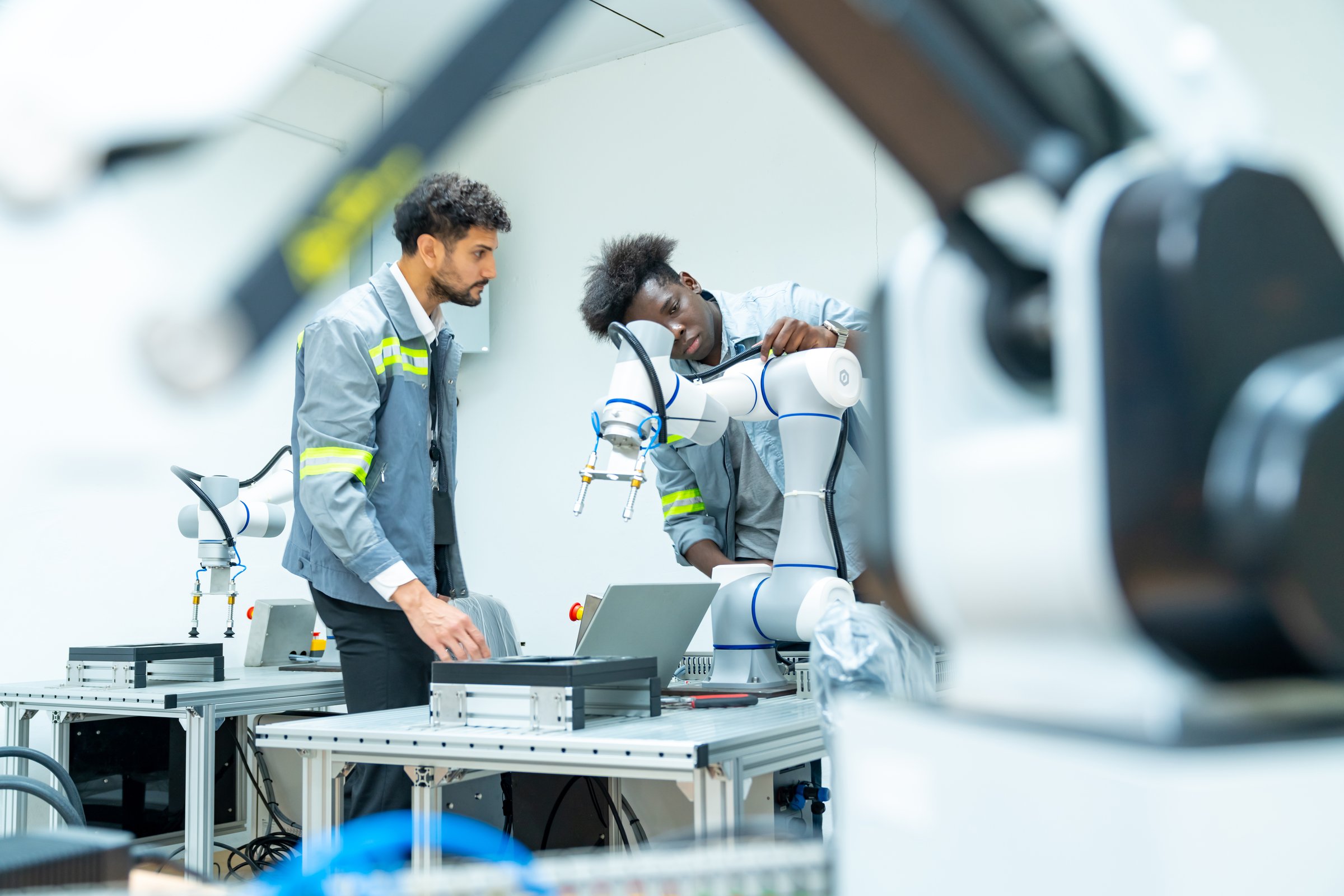 Manufacturing, industry technology and science concept. Male technician engineer teamwork checking and maintenance electric robotic machine arm system with computer software in factory laboratory.