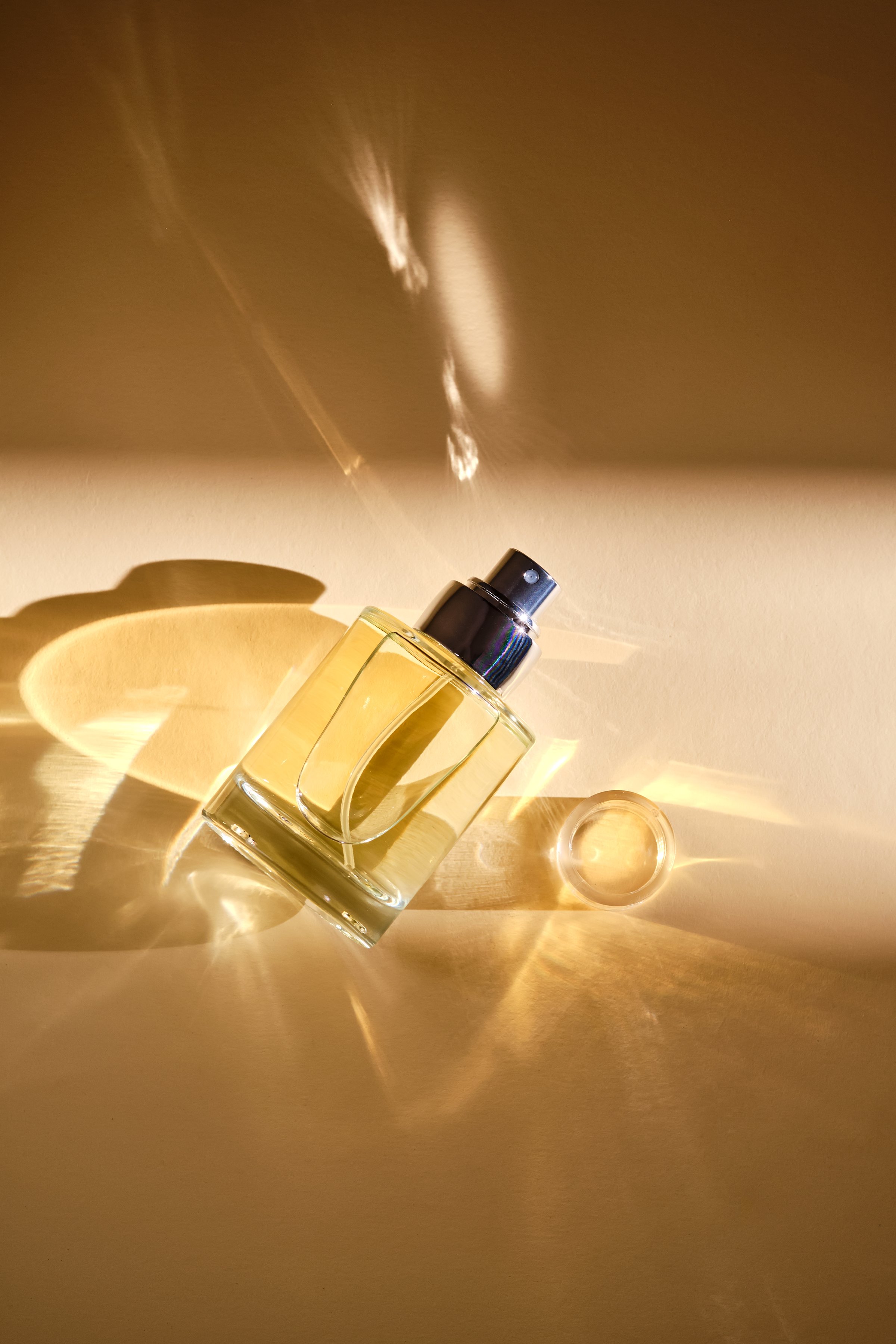 Perfume on a beige background in the rays of bright sun with beautiful highlights. High quality photo.
