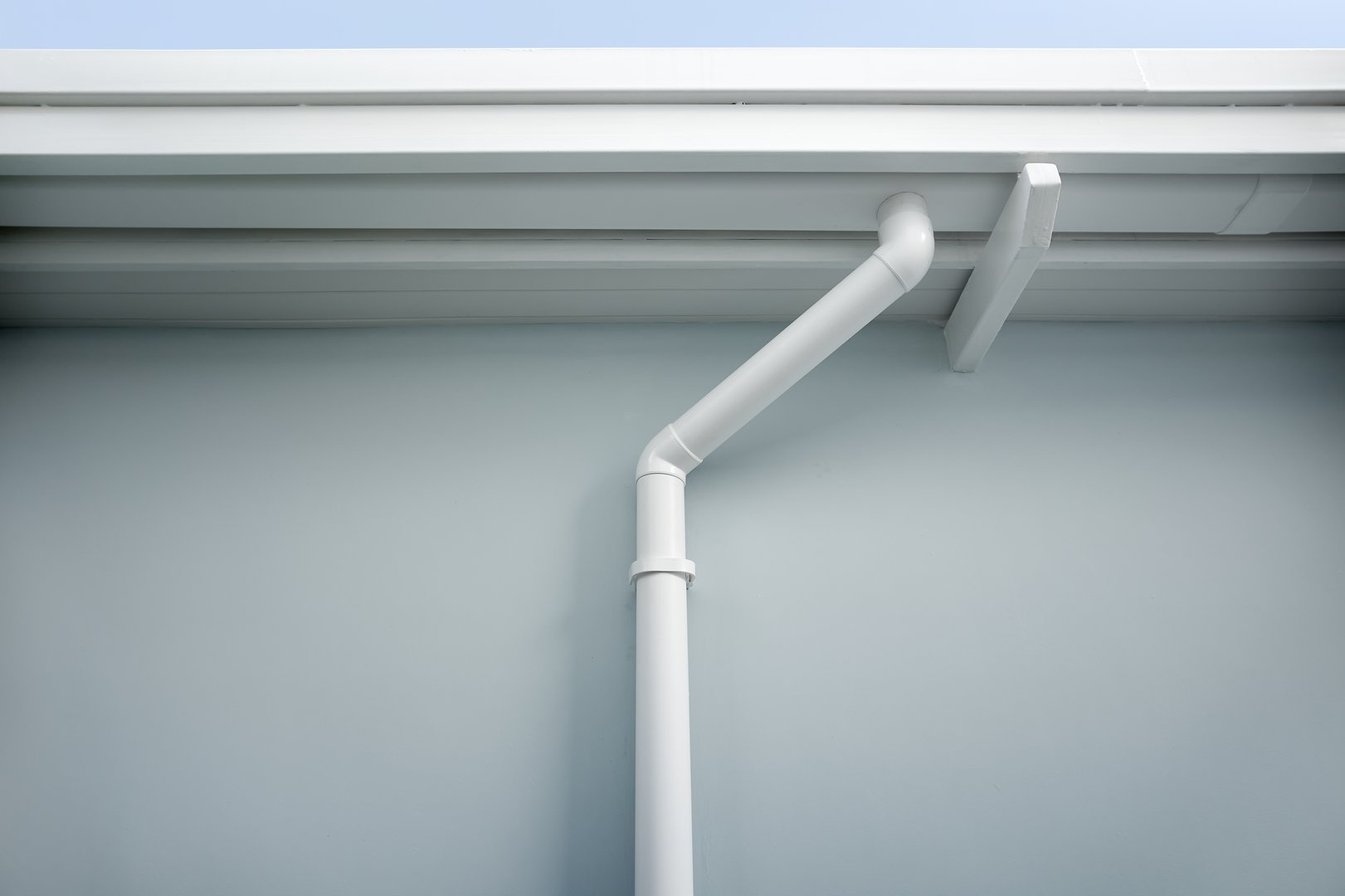Rain gutter install on steel structure, connect to pvc downpipe or downspout, elbow at eaves, exterior house building. Also called guttering or eavestrough for water drainage system. Look new clean.