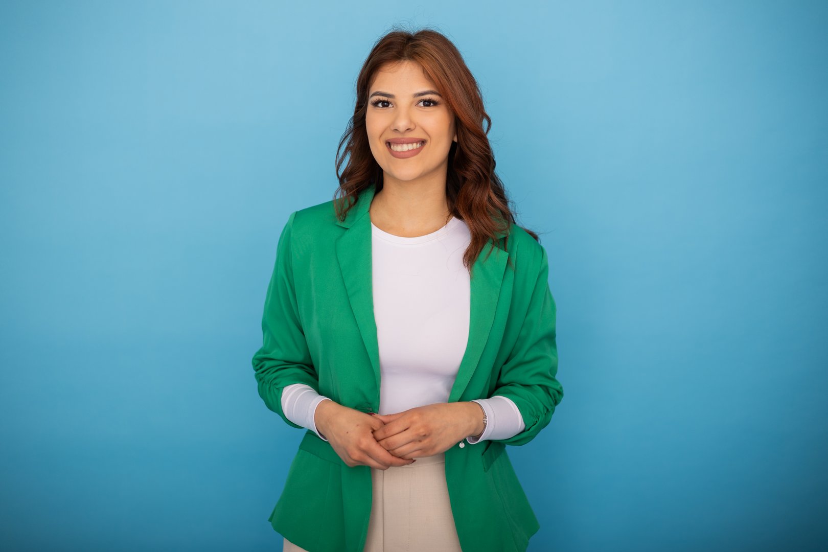 Portrait of a cheerful young businesswoman wearing a green jacket, posing on a vibrant blue background