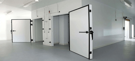 Industrial cold storage room with several open white doors, gray flooring, and bright lighting.