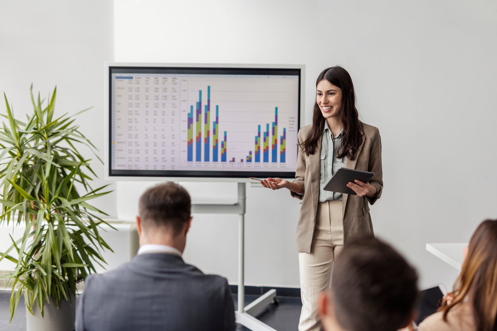 Portrait of smiling female data analyst standing at meeting room at corporate company with team of experts and having presentation with charts and graphs on white board.