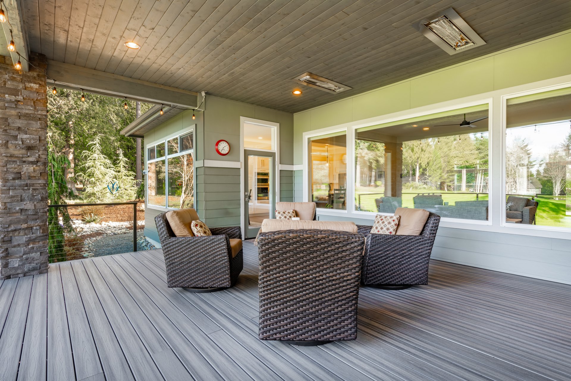 Beautiful custom built home with a modern contemporary style easy care landscaping grey siding white window trim large windows with view to a golf course in the pacific northwest. The home is set against a sunny blue sky and features a large covered deck patio with wicker furniture and a large bbq grill