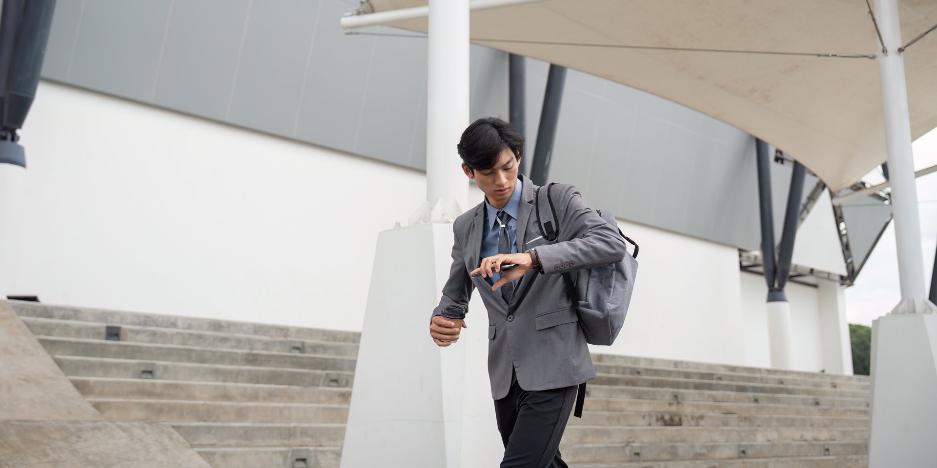 Asian businessman walking with a backpack while checking his watch, symbolizing a fast-paced lifestyle.