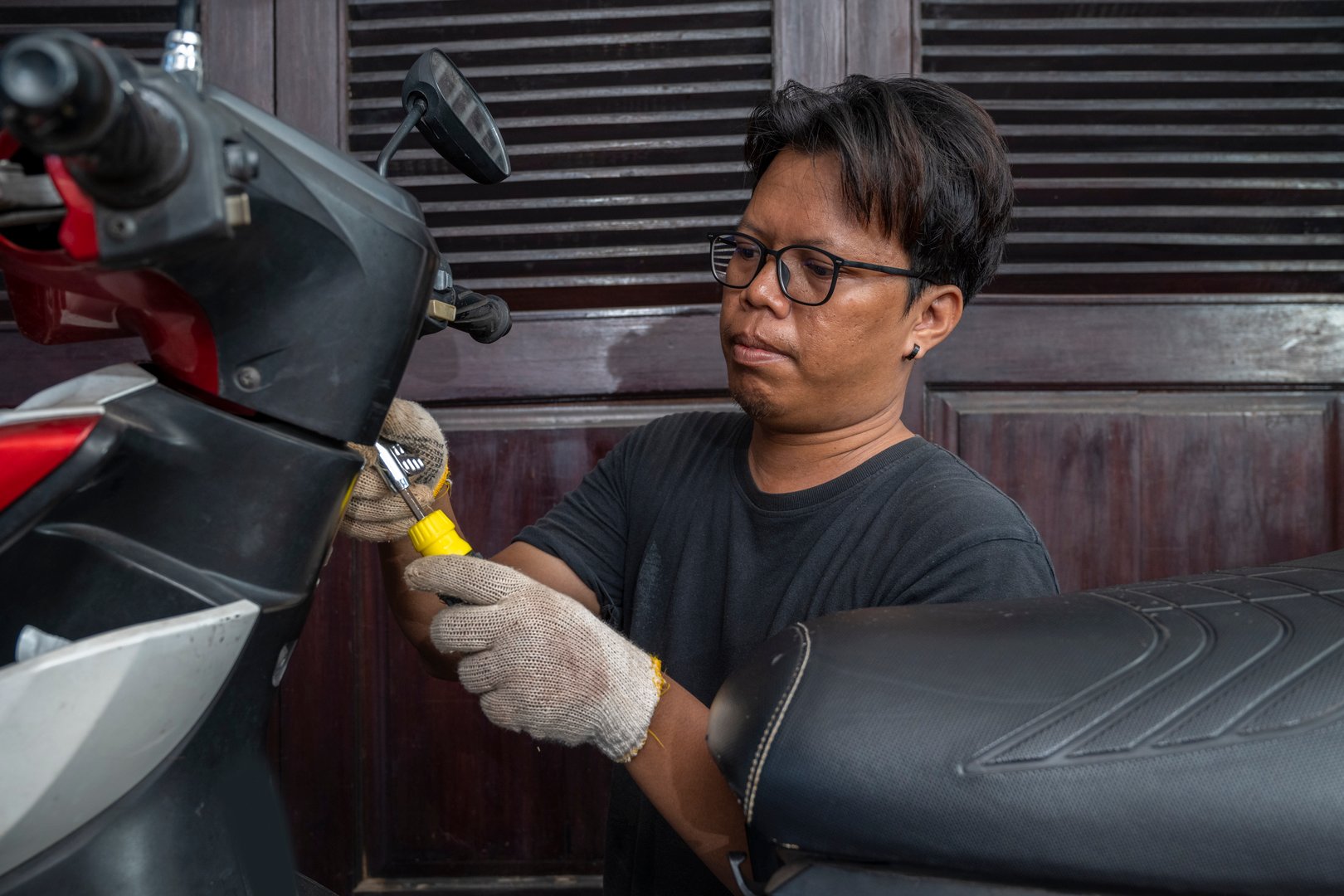 Indonesian southeast asian repairman using a socket screwdriver tool to repair a motorcycle in a workshop
