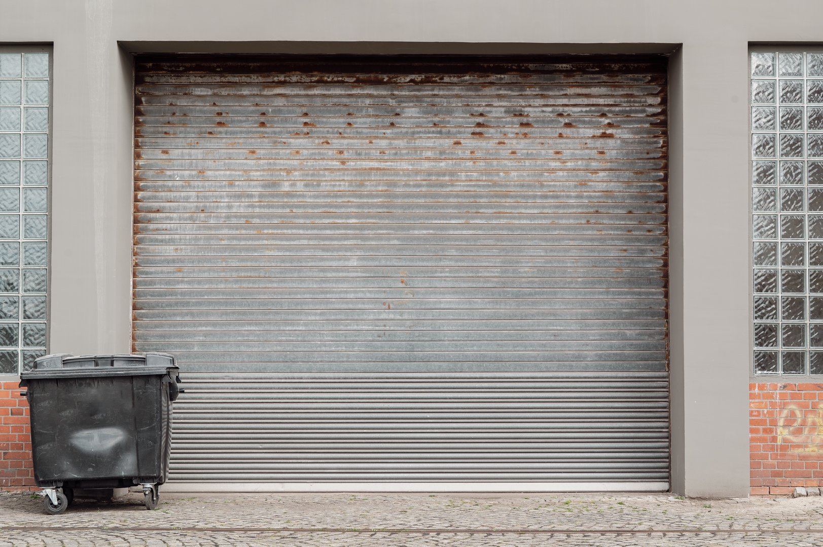 Close-up of a closed roller shutter door with a garbage container in front of a workshop