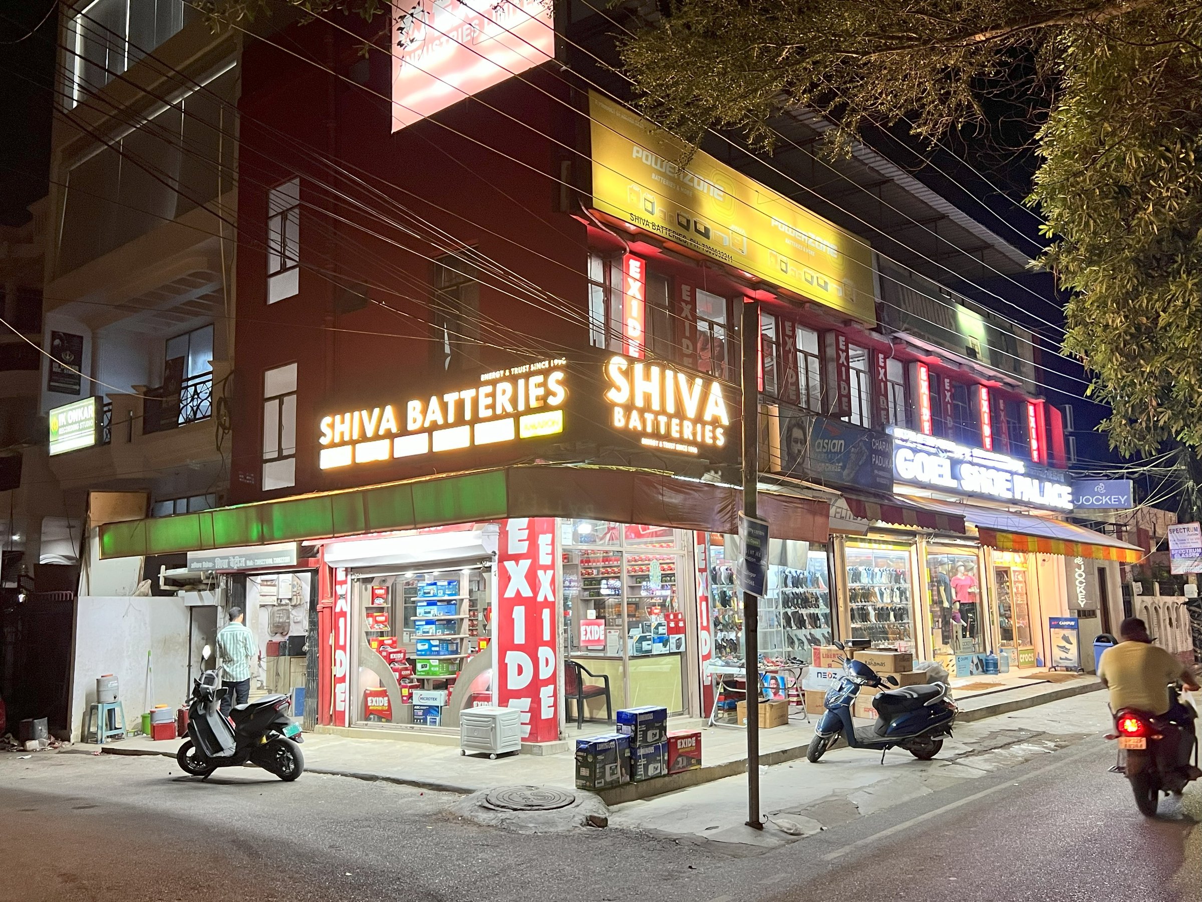 Street view of a brightly lit battery and gift shop at night with motorcycles parked outside.