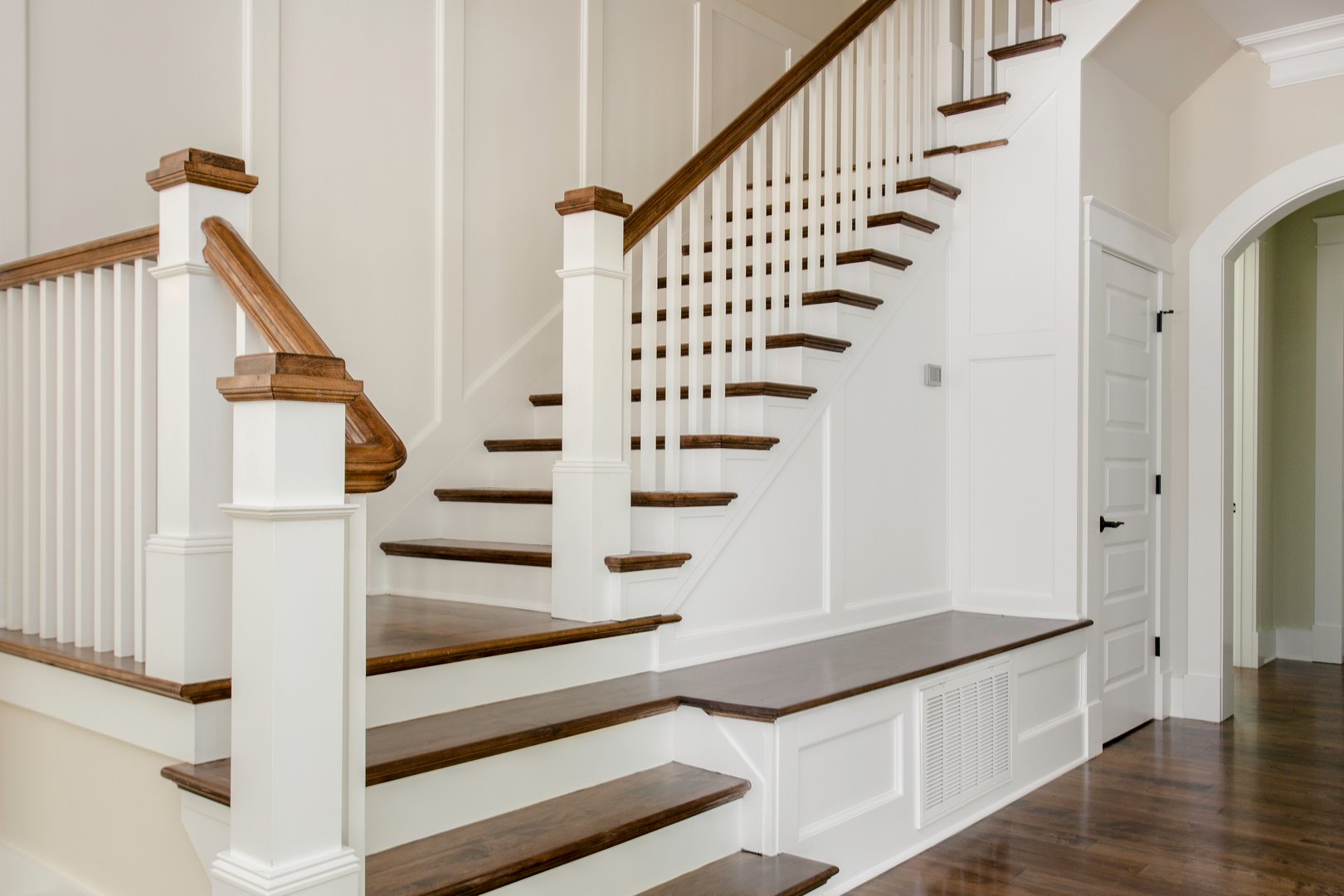 This image features a stylish and elegant staircase inside a modern home, complete with white railings and polished wooden steps.