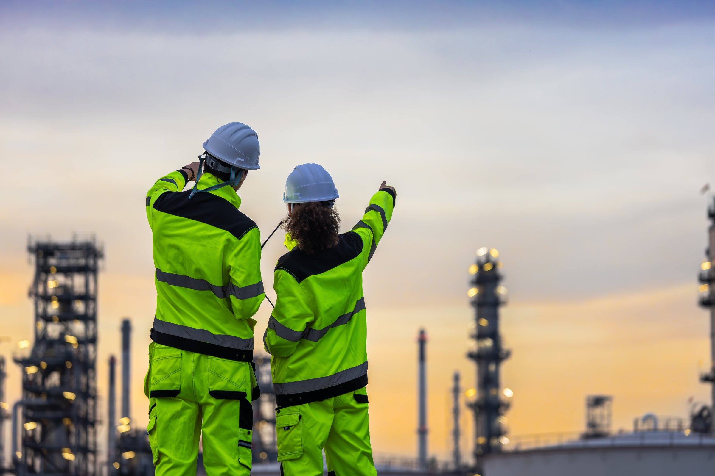 Workers Collaborating at Manufacturing Refinery Plant, Team of Engineers Reviewing Plans at Industrial Site at Dusk, Safety Engineers Surveying Refinery Operations
