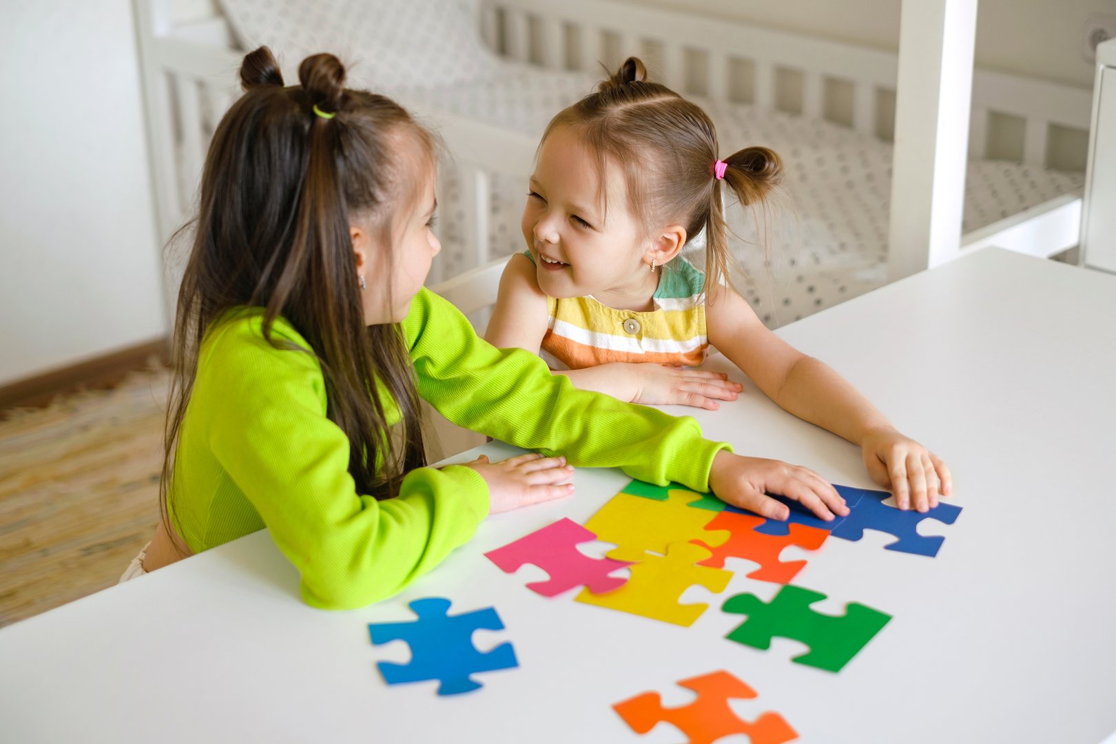 A young woman and a little girl play with educational toys at a preschool or daycare, engaging in learning activities with a shape sorter in a bright, cheerful classroom.