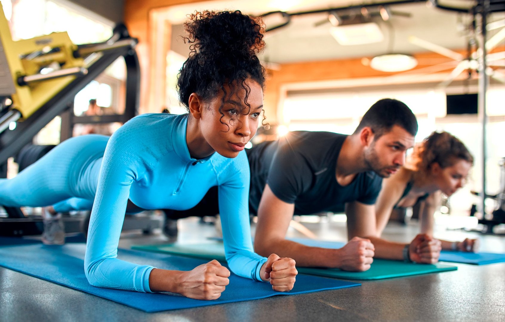 Slim women african american and caucasian ethnicity and muscular man in sportswear doing plank exercise on rubber mat in gym club. The concept of sports and recreation.