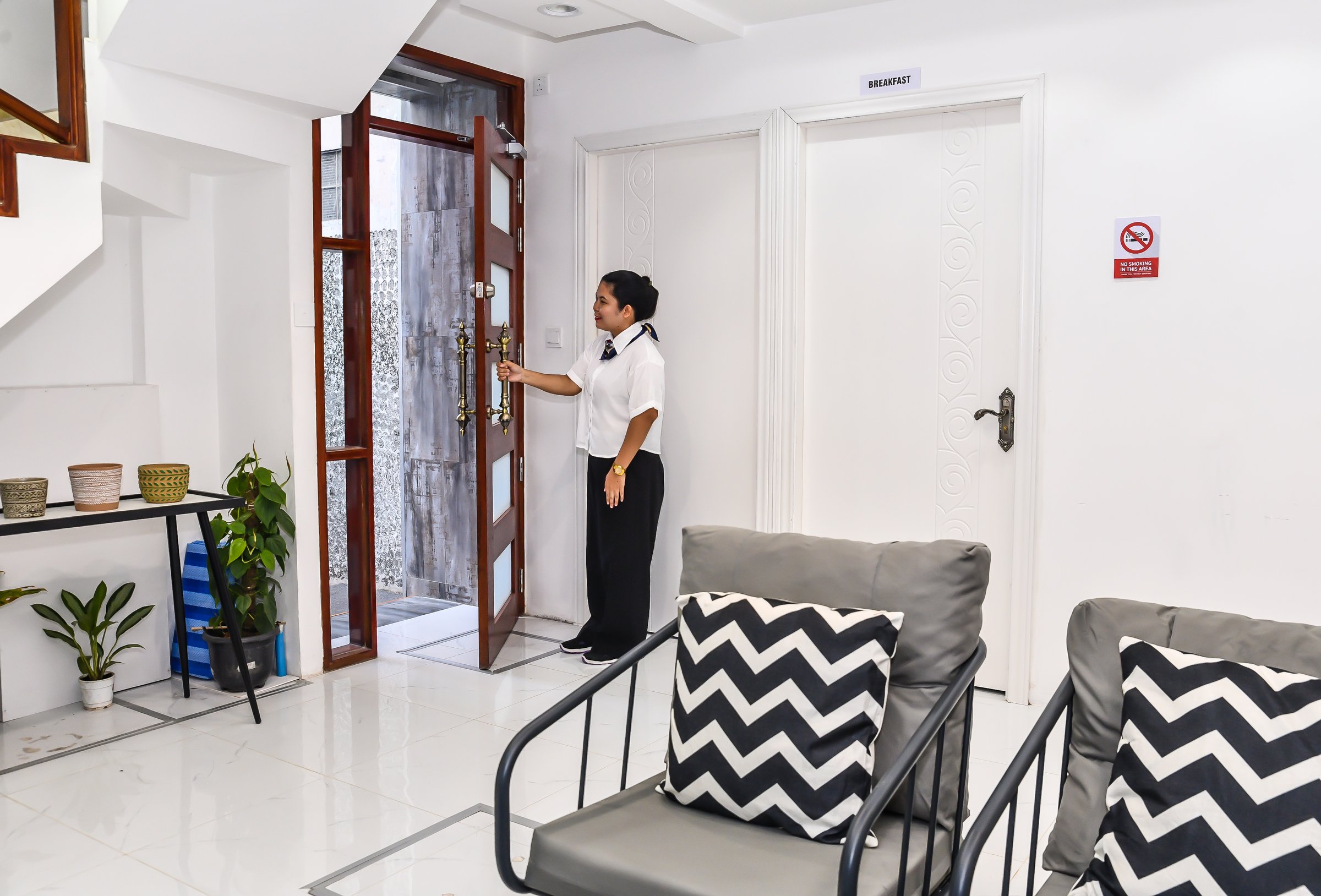 A security guard checks the lock of a glass door in a modern, stylish interior with plants and patterned cushions.