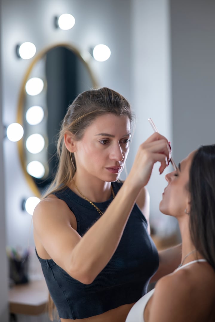Makeup artist carefully applies eyeshadow to model's eyelids with precision in a professional beauty environment.