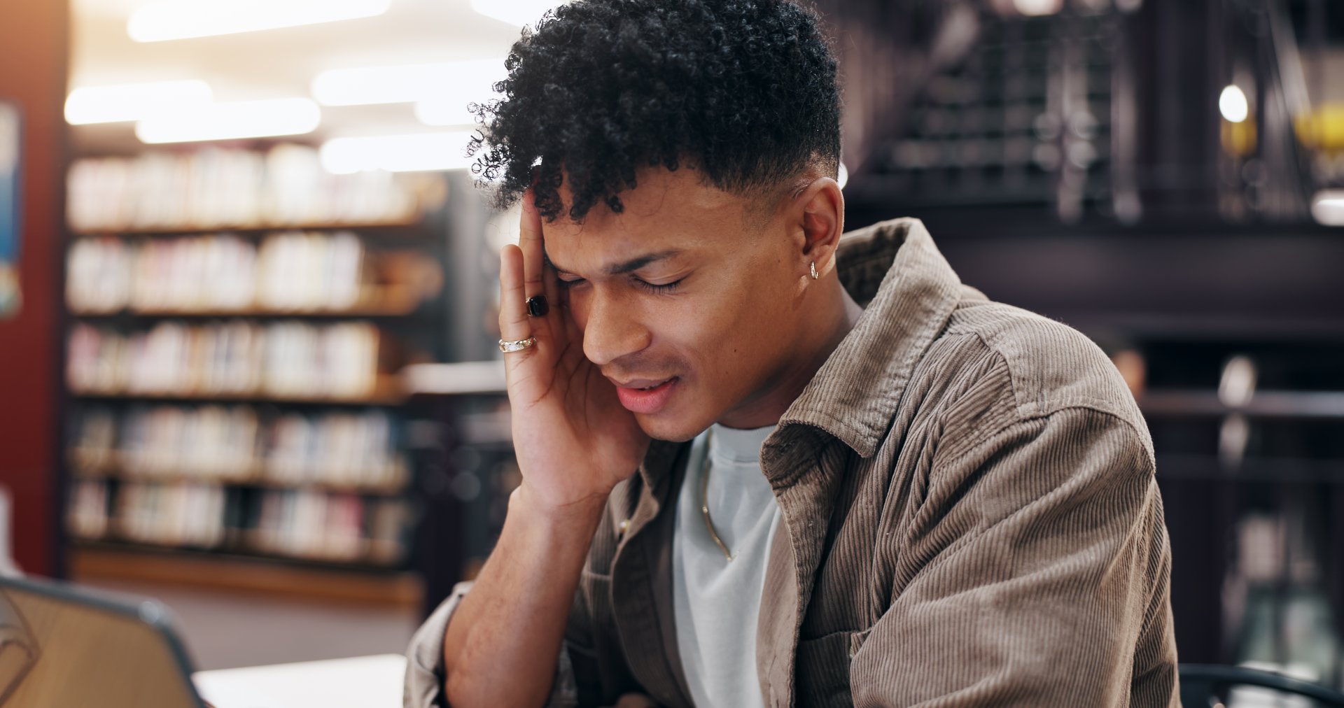 Man, student and tech in library with headache, stress and massage temple for relief. Person, laptop and migraine at university campus with fatigue, tension and tired with research or assignment