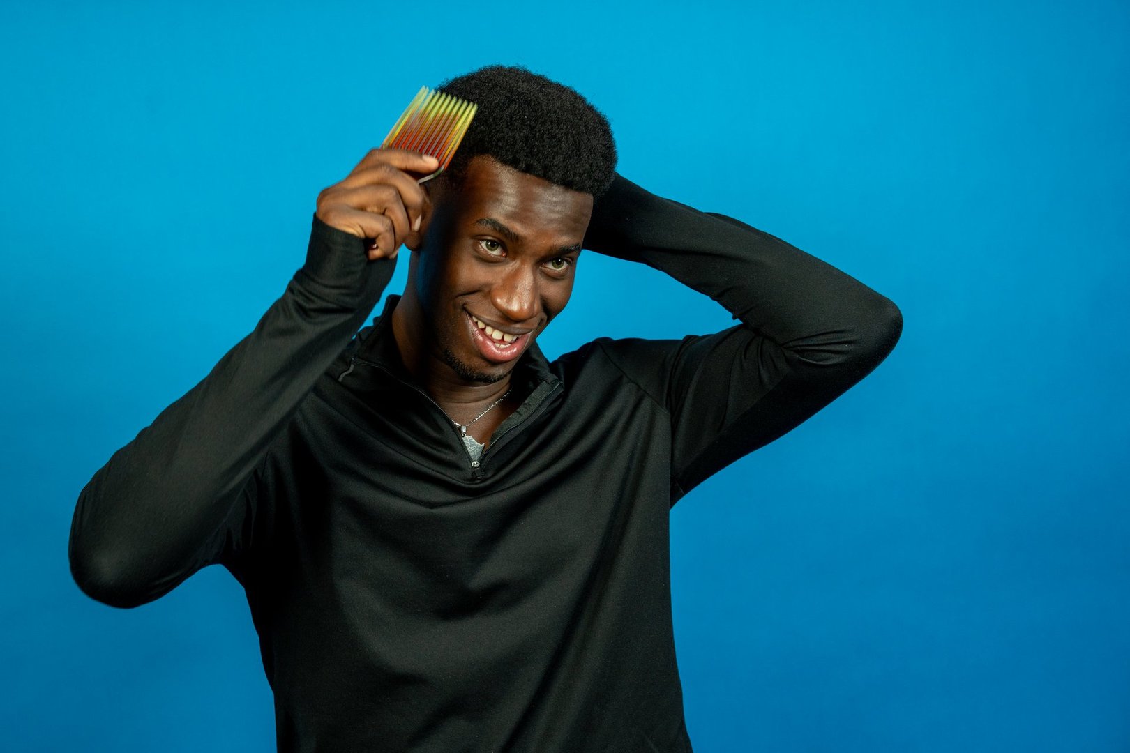Studio shot of a young black athlete combing his hair and smiling on a blue background