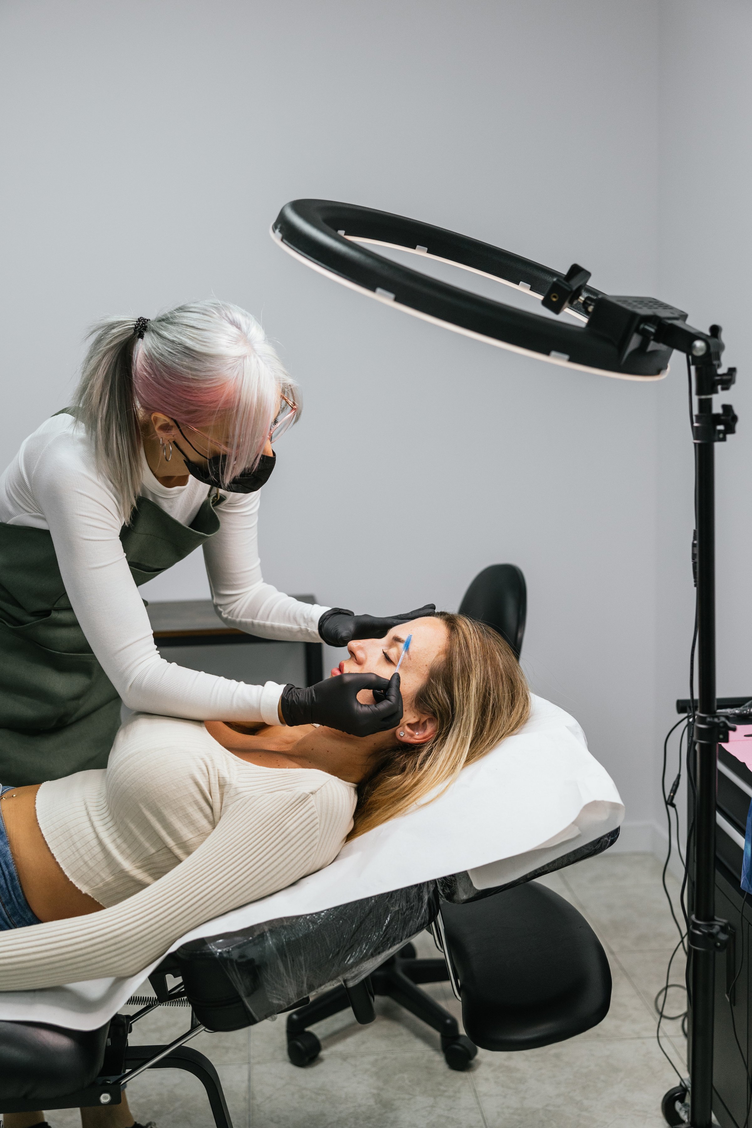 Beautician measuring and designing eyebrows of a client before microblading treatment in a beauty salon