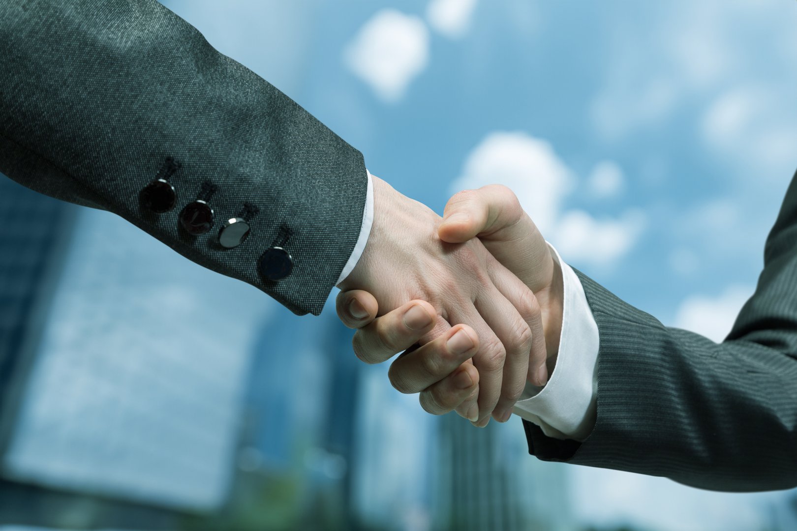 Business handshake signaling a successful partnership in urban setting. Two professionals shake hands celebrating a new business agreement against a city skyline.