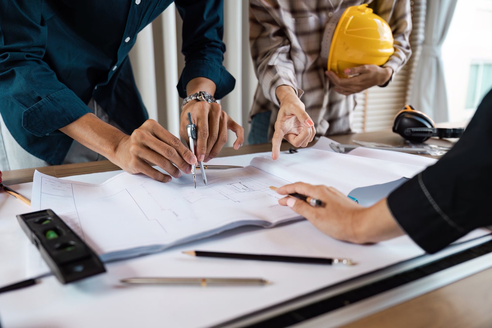 Architects working together on a blueprint, discussing plans with tools and safety gear, showcasing teamwork and collaboration in construction.