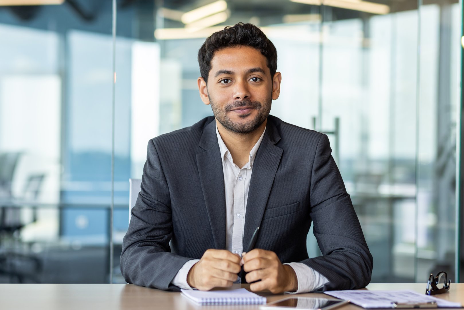 Portrait of a young investor banker at the workplace inside the bank office, a businessman in a business suit looking friendly at the camera, a man at work.