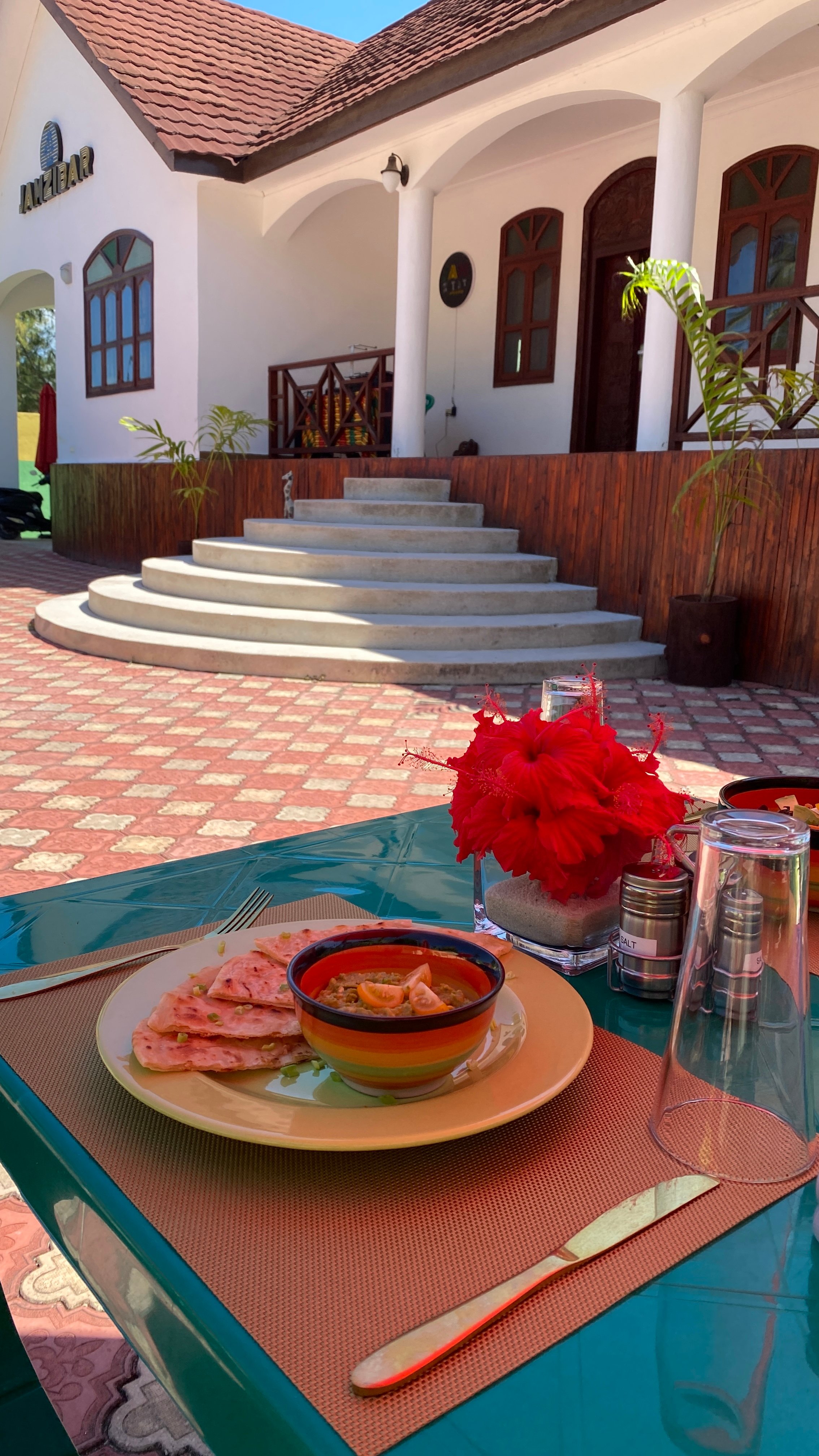 Outdoor dining scene with a plate of quesadillas and dip on a table, in front of a white building with arched windows.