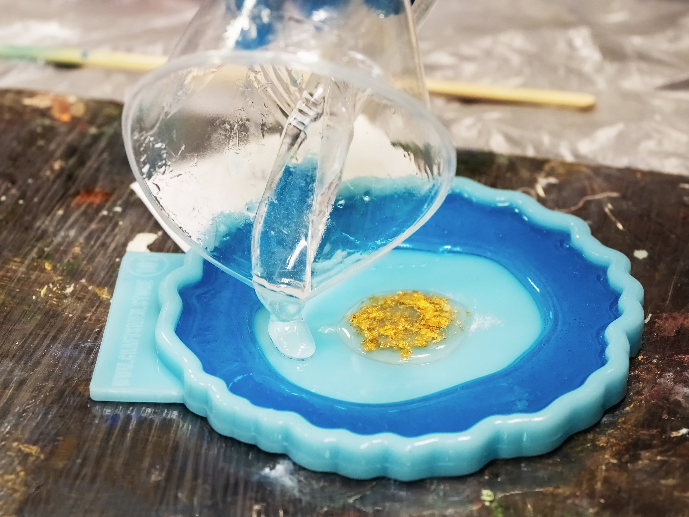 The art process of pouring epoxy resin into a golden toy. Technology process of creating a painting in style resin art, works with epoxy in studio, makes a wooden stand with the image. Close up.