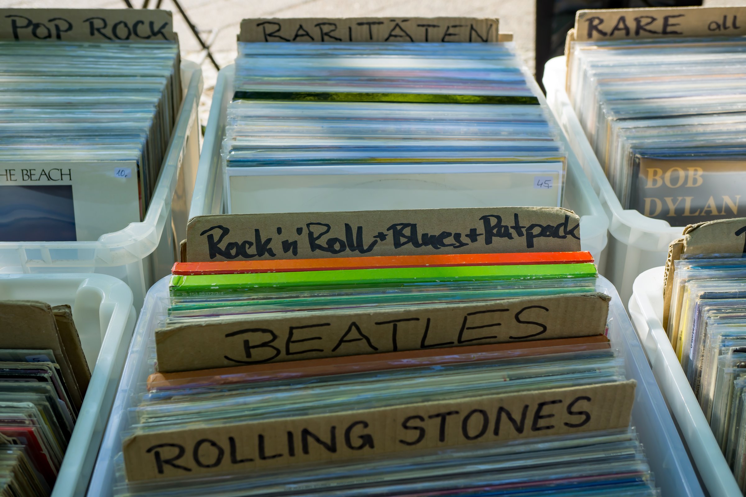 Neatly sorted vinyl records in plastic crates at a flea market in Berlin. Cardboard dividers label music genres and artists such as Rock'n'Roll, Blues, Beatles, and Rolling Stones. A nostalgic display for collectors and fans of analog music.
