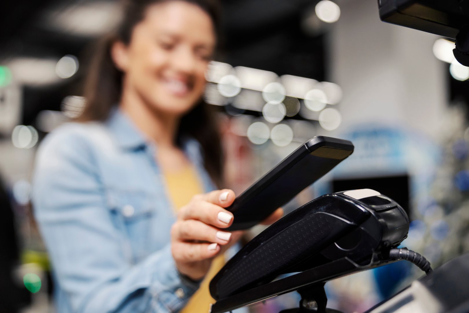 Close up of a female's hand paying bill on pos terminal with phone app at supermarket.