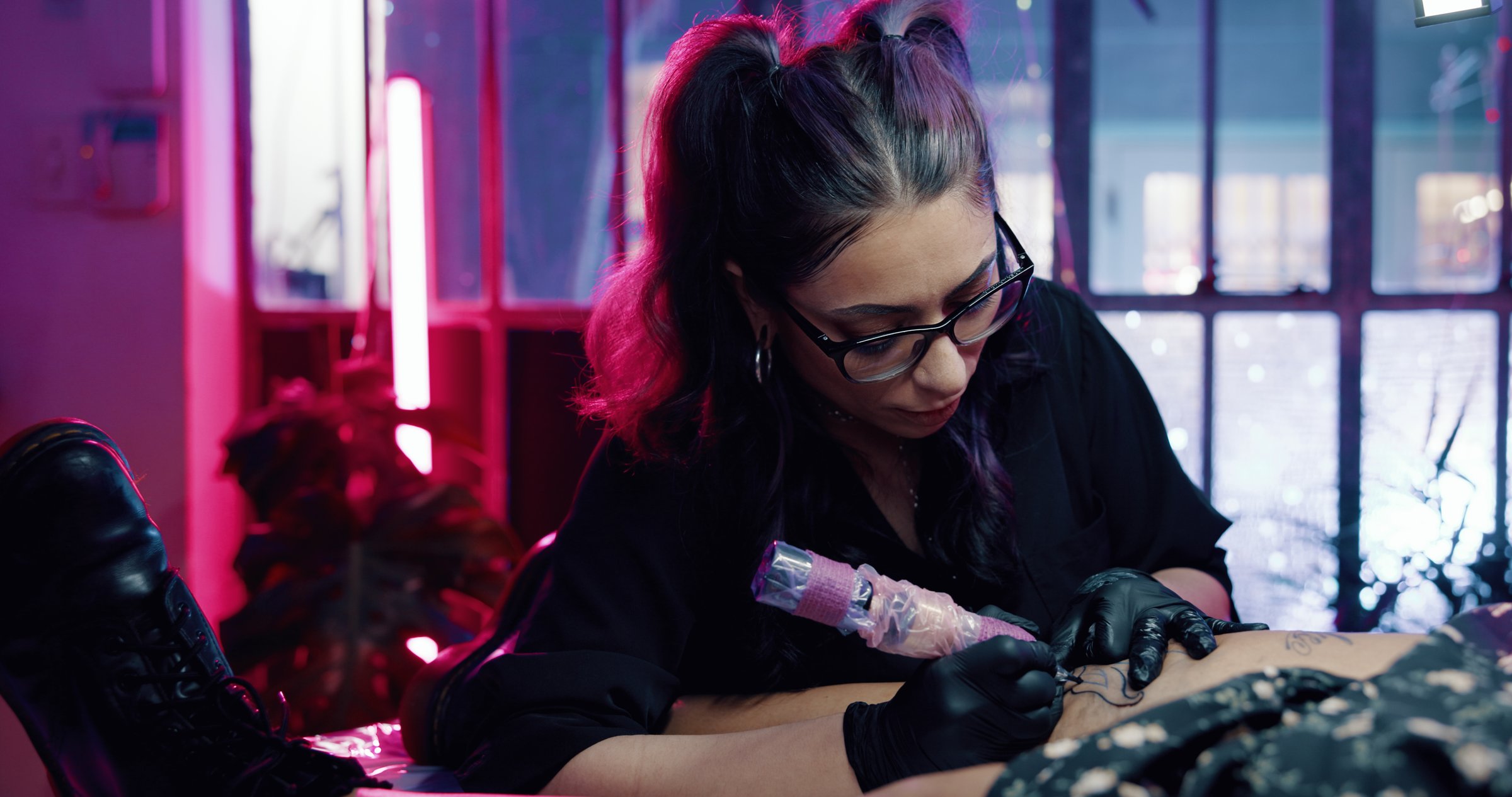 Tattoo, artist and leg with woman in store for permanent ink, linework design or aesthetic. Culture, self expression and tattooing parlor with person and customer in studio for identity and body art