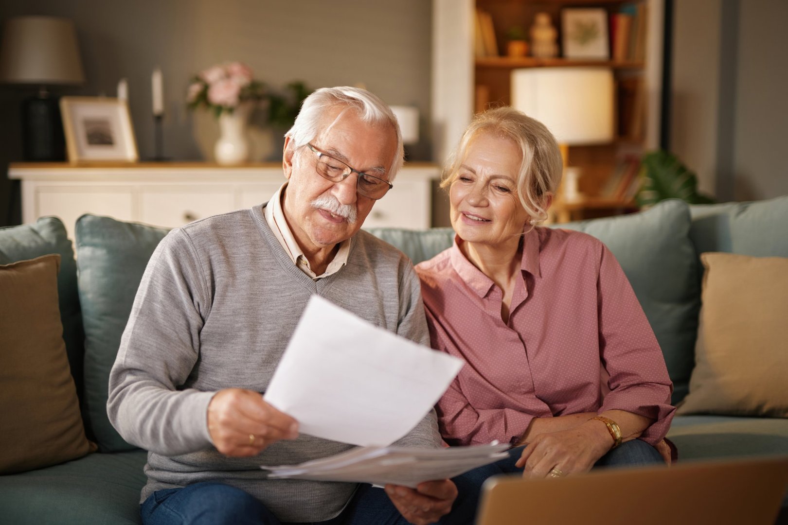 Happy retired couple reading their life insurance policy documents on the sofa at home