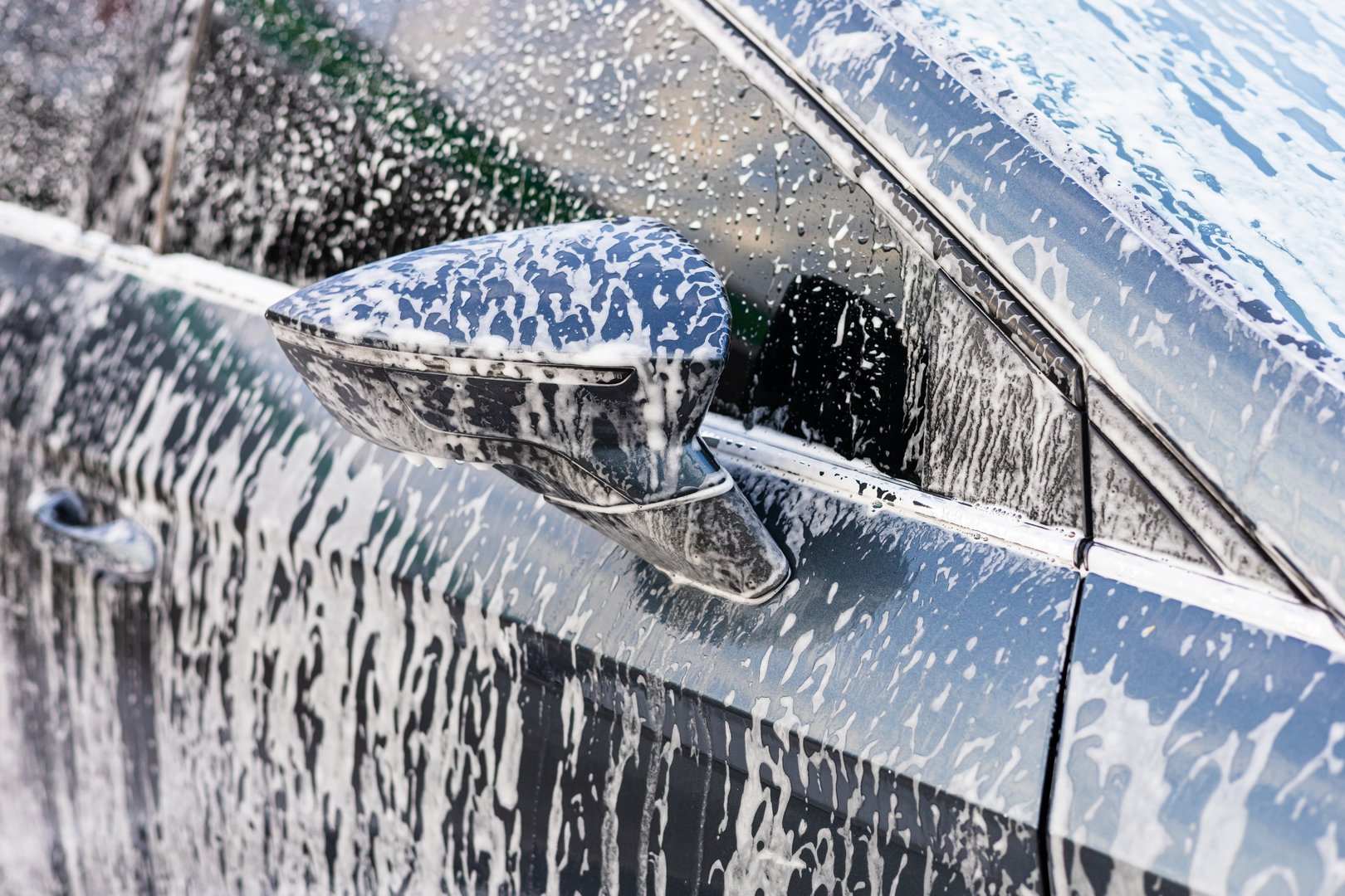 Self-service car wash. Bright sunlight reflects off soapy car windshield as bubbles and foam accumulate. peaceful atmosphere surrounds the driveway, indicating leisurely afternoon washing activity.