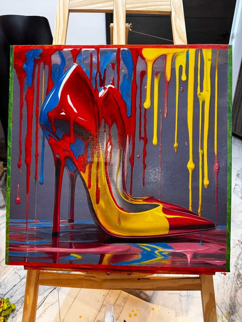 Painting of a high-heeled shoe with red, blue, and yellow paint dripping on a canvas on an easel.